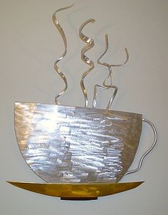 a metal sculpture with a coffee cup on it's side hanging from a wall