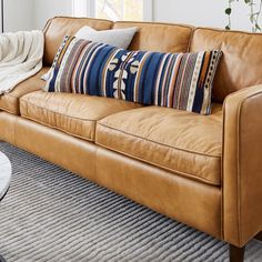 a brown leather couch sitting in a living room next to a window