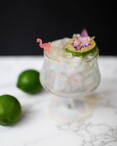 a small glass filled with ice and limes on top of a white marble table