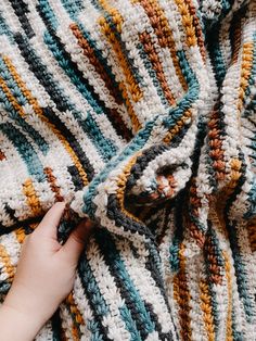 someone is crocheting on a blanket with their hand and the yarns are multicolored