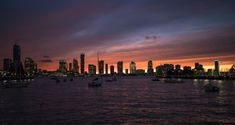 the city skyline is lit up at night as boats are in the water near it