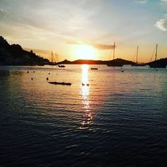 the sun is setting over some boats in the water