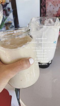 a hand holding a jar filled with white liquid next to another jar full of brown liquid