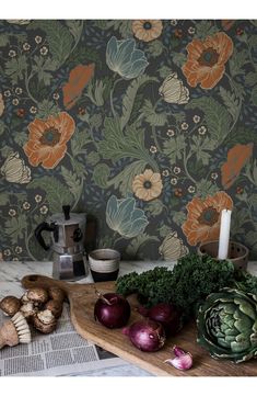 an assortment of vegetables on a cutting board next to a wallpapered wall with flowers