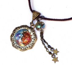 "A necklace with whimsical celestial charm featuring an embossed gold moon and sun pendant that's been accented with violet and pinked orange! Dangling alongside,a couple of star charms swing beneath a lustrous faceted glass bead of light turquoise! And a violet/moonstone-colored Swarovski crystal rhinestone sparkles from the half moons' chin! The artful pendant hangs from a faux suede necklace that has an extender chain to make it easy to find your perfect length! Add this one to your jewelry b Adjustable Celestial Charms Jewelry, Round Adjustable Necklace With Sun And Moon Design, Adjustable Necklace With Star Charm, Adjustable Round Sun And Moon Design Necklace, Whimsical Moon Charm Dangle Jewelry, Whimsical Dangle Moon Charm Jewelry, Whimsical Dangle Jewelry With Moon Charm, Whimsical Star Charm Jewelry As Gift, Whimsical Star Charm Jewelry Gift