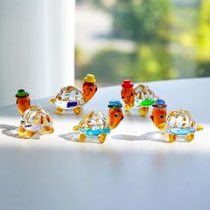 six glass figurines are sitting on a table next to each other, one is orange and the other is yellow