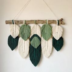 a wall hanging made out of wood and knitted leaves on a white wall background