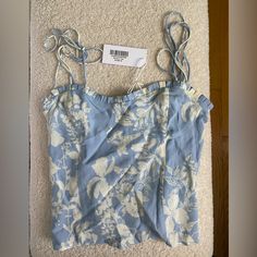 a blue and white top with flowers on it sitting on the floor next to a hanger