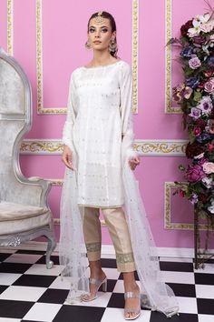 White and gold are preferred choices of Mughal princess. You can never go wrong with a classy white silhouette. Sylvia by Maria Nasir is a classic wardrobe piece for a reason! This elegant piece defines femininity and can make you look beautiful effortlessly. Sylvia is beautiful combination of pearl white and gold A-line shirt in paper cotton fabric. The boat neckline is dazzled with gold lace while the ¾ sleeves are also adorned with gold lace. Featuring the soft organza tulle dupatta in shades of pearl white and gold. The shirt is paired with a matching silk slip and beige pants with lace detailing. Accessorize this number with ethnic earring and bindya set for a flawless look. Top: Color: White Fabric: Paper cotton A shaped shirt with zari work all over Boat shaped neckline    Gold lace Elegant Churidar With Sheer Dupatta For Navratri, Celebration Kurta With Dupatta In Tissue Silk, Tissue Silk Kurta With Dupatta For Celebration, Celebration Kurta With Sheer Dupatta In Raw Silk, Elegant Sets With Sheer Dupatta For Celebration, Gold Long Sleeve Dresses For Diwali, White Tissue Silk Kurta With Sheer Dupatta, Elegant Churidar With Chikankari Embroidery In Art Silk, White Raw Silk Dress For Navratri