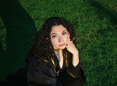 a woman laying in the grass with her hand on her face and looking at the camera