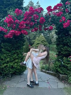 two girls are hugging each other in front of pink flowers