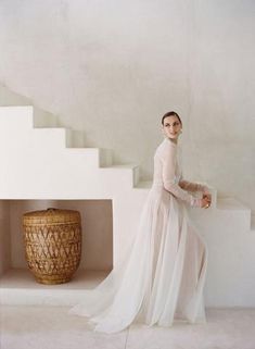 a woman in a white dress is standing on some stairs with a basket and vase