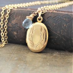 "A lovely gold filled locket graces this necklace. The vintage piece has classic swirled etched on the front; the back is plain. The 12k gold filled pendant is hallmarked on the inside which has two frames to place your beloved photos beneath. The locket has been set on a new 14k gold filled chain and paired with a wire wrapped aquamarine briolette (March birthstone). The necklace is finished with a lobster clasp. Locket 26x17mm Necklace 18\" (45cm) ✦All of our vintage lockets ship with complime Vintage Charm Oval Link Necklace As Gift, Elegant Jewelry With Vintage Charm And Oval Link, Elegant Vintage Charm Oval Link Jewelry, Gold Heirloom Brass Locket Necklace, Dainty Gold Oval Locket Necklace, Oval Link Necklaces With Vintage Charm For Gifts, Heirloom Gold Brass Locket Necklace, Gold Locket For Vintage Jewelry Collection, Vintage Necklace With Engraving Option For Keepsake