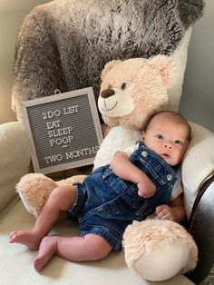 a baby sitting on a chair with a teddy bear and sign that says, do list eat flesh for two months