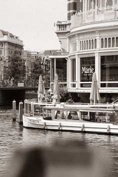 there is a boat on the water in front of a building with umbrellas and tables