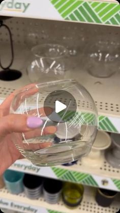 a person is holding a clear glass bowl in their hand and it's on the shelf