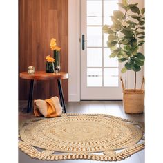 a round rug on the floor next to a table and potted plant in front of a door