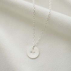 "A dainty silver coin is delicately suspended on a sterling silver necklace chain, and hand stamped with an uppercase letter of your choice. Add on additional coins personalized with letters of your choice, or a heart symbol. Hand stamped to order in our Vancouver studio. *Free shipping for orders to USA and Canada, and no duties or customs fees.* > Sterling silver coin is 9mm in diameter > Shown worn on a 16\" satellite chain > Comes beautifully packaged and ready for gift giving > Dainty Hand Stamped Charm Necklaces For Everyday, Dainty Hand Stamped Charm Necklace For Everyday, Dainty Round Charm Necklace As Gift For Mom, Dainty Round Charm Necklace For Mom, Everyday Meaningful Sterling Silver Charm Necklaces, Everyday Meaningful Sterling Silver Charm Necklace, Simple Charm Necklaces For Mother's Day, Stamped Sterling Silver Heart Pendant Necklace, Dainty Hand Stamped Round Disc Necklaces