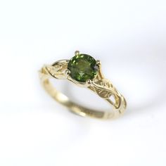 a gold ring with a green stone in the center and leaves around it, on a white background