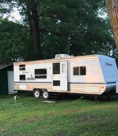 an rv parked in the grass next to a tree and shed with its door open