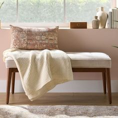 a bench with a blanket on it in front of a window and bookshelf