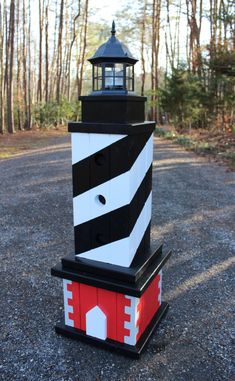 a black and white lighthouse sitting on top of a gravel road in front of trees