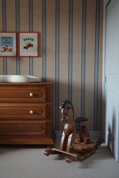 a wooden rocking horse next to a dresser with striped wallpaper in a child's room