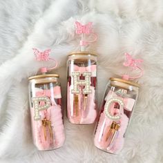 three glass jars filled with pink and gold items on top of a white fur rug