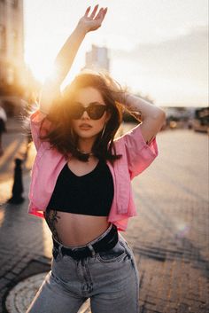 a woman wearing sunglasses and a crop top poses for the camera with her arms in the air