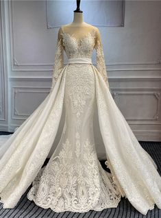 a white wedding gown with long sleeves and a train on display in a room full of mannequins