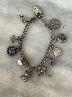 Vintage British silver charm bracelet. Made in the UK between the late 1950s  and early 1970s. The bracelet is fairly light, as are the charms,  making it suitable for a girl to wear. It has 10 charms: '21', shell, Pisces medallion,  boot, poodle, teddy bear, Swiss chalet, evil  eye, anchor, Cornish pinkie. The bracelet is 0.6 cm wide, and 18.5 cm long. The clasp is a heart-shaped 'gate clasp', with  safety chain. Condition is excellent, used. Vintage Dangle Charm Bracelet, Silver Vintage Charm Metal Charms, Silver Vintage Metal Charms, Silver Metal Charms With Vintage Detail, Vintage Dangle Charm Bracelet As A Gift, Vintage Dangle Charm Bracelet For Gifts, Vintage Dangle Charm Bracelet Gift, Silver Charm Bracelet With Logo For Gift, Silver Charm Bracelet With Logo As Gift