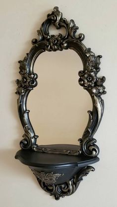 an ornate mirror hanging on the wall above a shelf with a black top and bottom