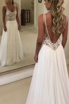 a woman in a wedding dress looking at herself in the mirror with her back to the camera