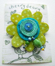 a brooch with green and blue beads on it's center, sitting on top of a piece of paper