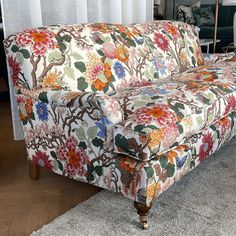 a floral couch sitting on top of a rug in front of a white curtained window