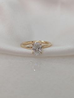 a gold ring with a single diamond on it sitting on a white satin material background