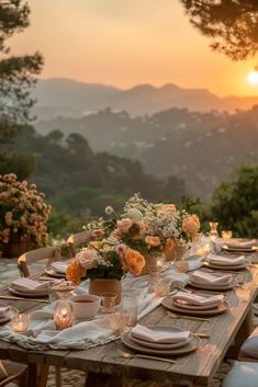 a wooden table topped with lots of white plates and place settings in front of a sunset