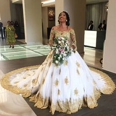 a woman in a white and gold wedding gown standing on the floor next to a flower bouquet