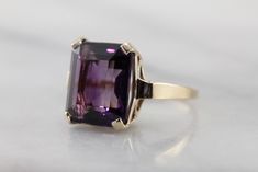 Classic elegance! We've completely restored this vintage, yellow gold mounting and set it with a gorgeous new amethyst of the deepest shade of aubergine purple! The bold but simple style of this ring allow it to be worn for a variety of occasions, from a day to day signature piece to an eye-catching accessory for the finest gown. Metal: 14K Yellow Gold Gem: Amethyst 9.55 Carats Gem Measurements: 13.9 x 11.9 mm, Rectangle Emerald Cut Ring Size: 7.25 Marks: "JAM14K" Stamped on the inside band Formal Purple Amethyst Ring In 14k Gold, Formal 14k Gold Purple Amethyst Ring, Classic Amethyst Purple Rings, Classic 14k Gold Purple Amethyst Ring, Purple Sapphire Ring With Prong Setting For Formal Occasions, Timeless Formal Amethyst Ring, Classic Yellow Gold Solitaire Amethyst Ring, Classic Purple Sapphire Ring With Prong Setting, Formal Purple Amethyst Solitaire Ring