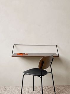 a desk with a black chair and a white wall in the background, next to it is a shelf that holds an orange object