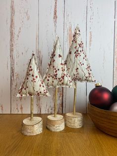 three small christmas trees sitting on top of a wooden table next to balls and ornaments