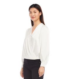 a woman standing in front of a white background wearing black pants and a white blouse