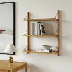 a wooden shelf with books on it next to a lamp and painting hanging on the wall