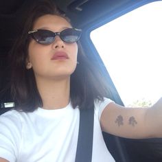 a woman wearing sunglasses sitting in the back seat of a car with her arm tattooed