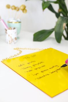 a yellow piece of paper with writing on it and a pink flower in the background