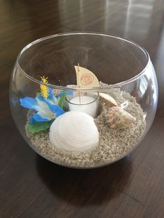 a glass bowl filled with sand, shells and seashells on top of a wooden table