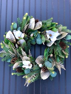 a wreath with white flowers and greenery on a blue door frame is hanging on the wall