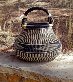 a black and white basket sitting on top of a stone wall next to some grass