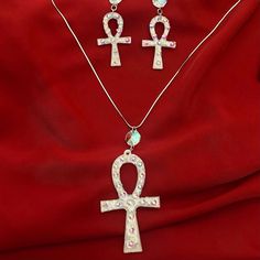 Our Ankh earring and necklace set is a stunning fusion of timeless symbolism and modern craftsmanship, meticulously crafted to embody the essence of elegance and mystique. At the heart of each piece lies the iconic Ankh symbol, revered in ancient Egyptian culture as a symbol of life and eternity. Sculpted with precision from luminous silver white mica, every Ankh pendant emanates a celestial glow, reminiscent of moonlit whispers on a tranquil night. Enveloped in hand-poured resin, the Ankh is lovingly encased, preserving its significance and beauty for generations to come. Delicate veins of silver leaf delicately adorn the edges, enhancing the ethereal allure of the design, while tiny rhinestones add a touch of celestial sparkle, reminiscent of stars scattered across a velvet sky. The earr Spiritual Crystal Jewelry Gift, Spiritual Crystal Jewelry For Gifts, Spiritual Crystal Jewelry As A Gift, Elegant Ankh-shaped Metal Jewelry, Nickel-free Ankh Elegant Jewelry, Symbolic Metal Jewelry With Matching Earrings, Nickel-free Ankh Shaped Elegant Jewelry, Silver Crystal Spiritual Jewelry, Elegant Nickel-free Ankh Jewelry