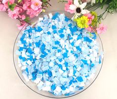 blue and white mosaic tiles in a glass bowl next to pink flowers on a table